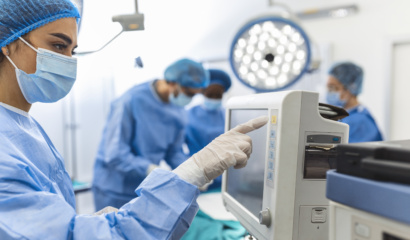 Diverse Team Of Professional Surgeons Performing Invasive Surgery On A Patient In The Hospital Operating Room. Nurse Hands Out Instruments To Surgeon, Anesthesiologist Monitors Vitals.