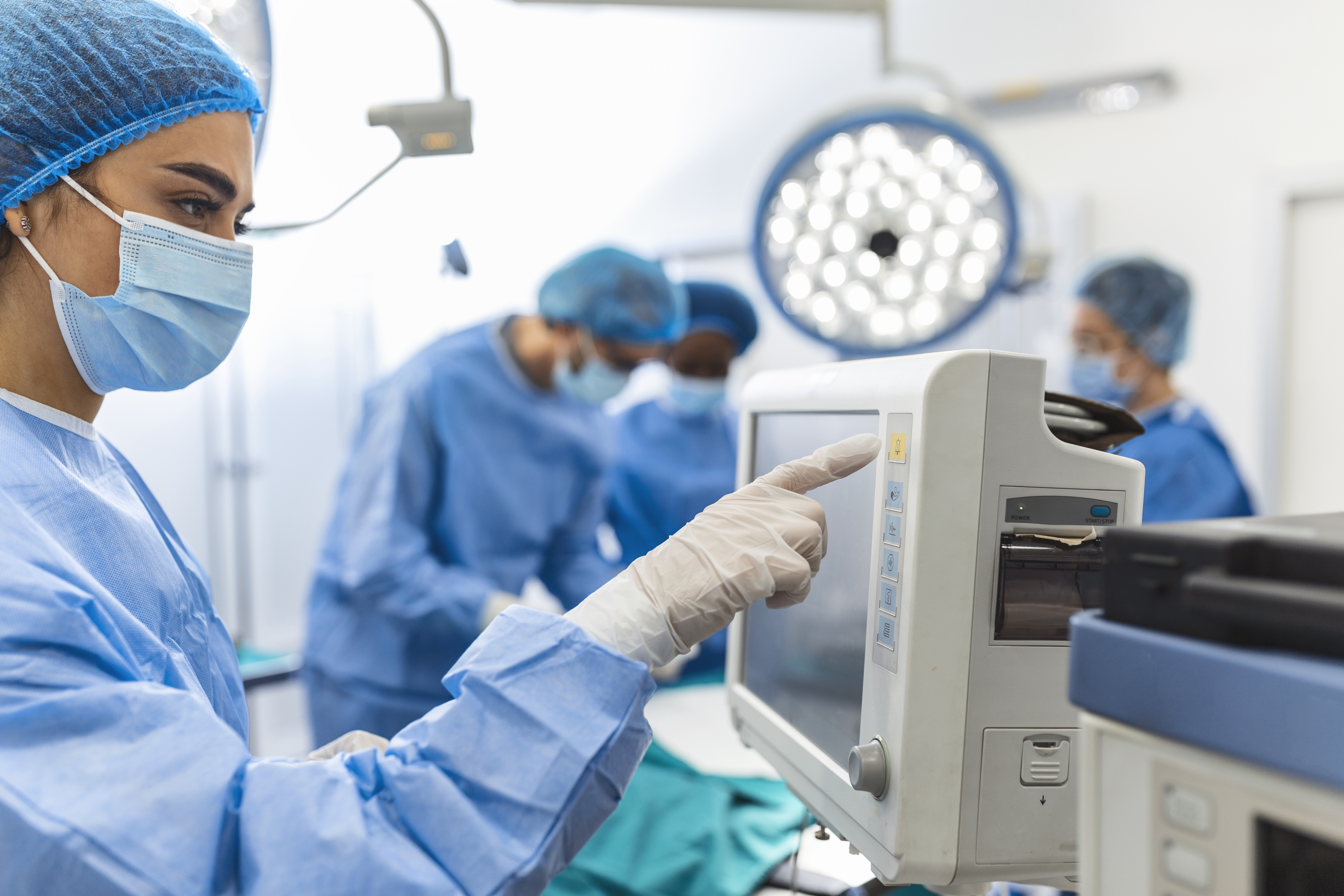 Diverse Team Of Professional Surgeons Performing Invasive Surgery On A Patient In The Hospital Operating Room. Nurse Hands Out Instruments To Surgeon, Anesthesiologist Monitors Vitals.